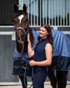 Woman in equestrian attire standing next to a horse wearing a blue blanket. equestrian fashion outfitters