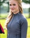 Woman wearing a gray long-sleeve top outdoors with greenery in the background equestrian fashion outfitters