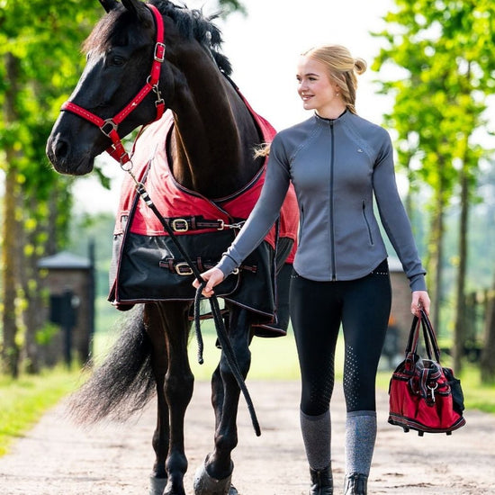 Woman walking a horse on a path with greenery in the background equestrian fashion outfitters