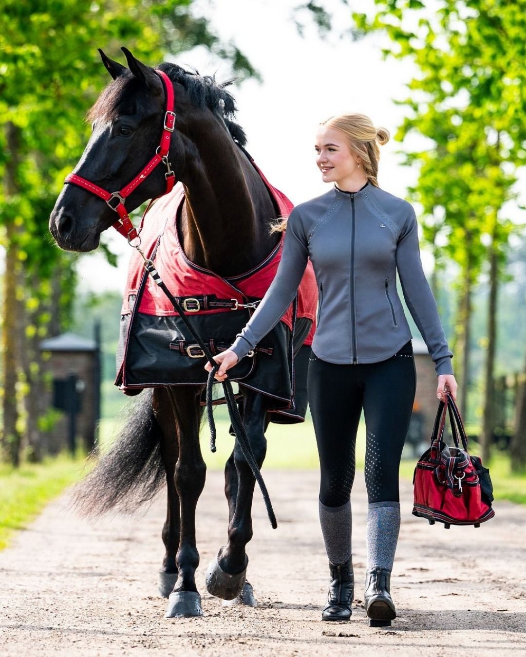 Woman walking a horse on a path with greenery in the background equestrian fashion outfitters