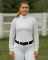 Woman wearing a white long-sleeve show shirt top and white pants with a black belt, standing outdoors. equestrian fashion outfitters