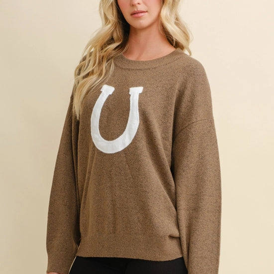 Woman wearing a brown sweater with a white horseshoe design on a beige background - equestrian fashion outfitters