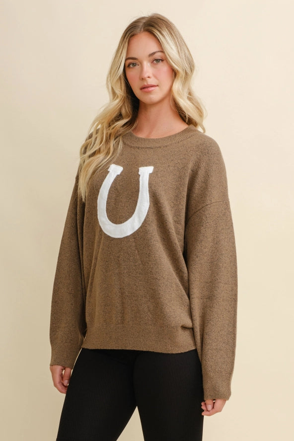 Woman wearing a brown sweater with a white horseshoe design on a beige background - equestrian fashion outfitters