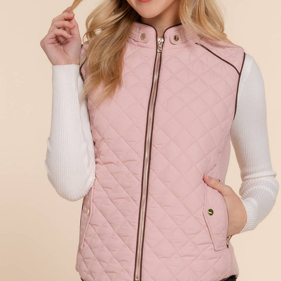 Woman wearing a pink quilted vest over a white long-sleeve shirt on a beige background equestrian fashion outfitters