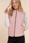 Woman wearing a pink quilted vest over a white long-sleeve shirt on a beige background equestrian fashion outfitters
