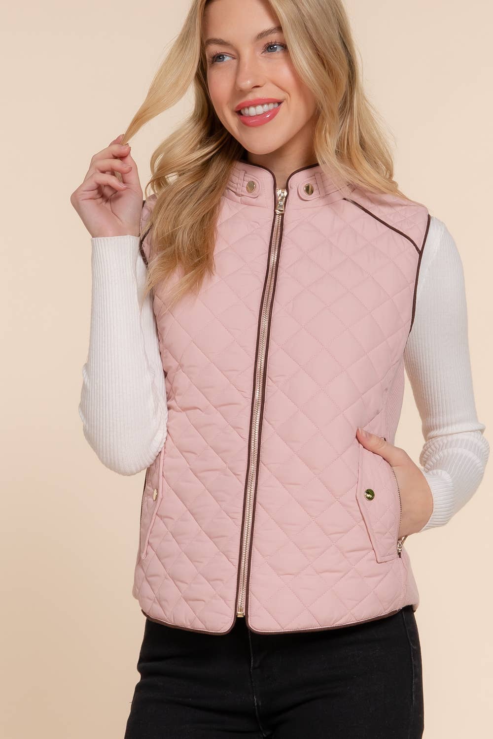 Woman wearing a pink quilted vest over a white long-sleeve shirt on a beige background equestrian fashion outfitters