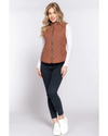 A woman modeling a rust-brown camel quilted sleeveless zip-front vest over a white long-sleeve top, black skinny pants, and white slip-on shoes, equestrian fashion outfitters