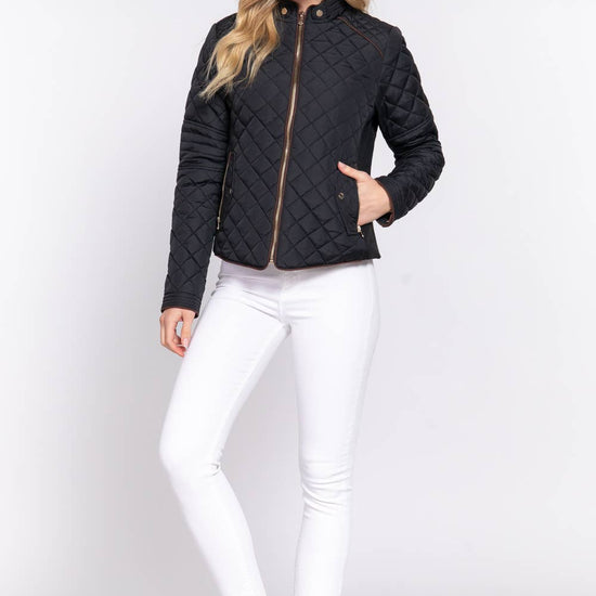 Woman wearing a black quilted jacket and white pants on a light gray background equestrian fashion outfitters