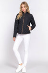 Woman wearing a black quilted jacket and white pants on a light gray background equestrian fashion outfitters