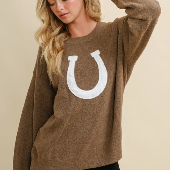 Woman wearing a brown horseshoe pullover sweater with a white horseshoe design on a beige background - equestrian fashion outfitters