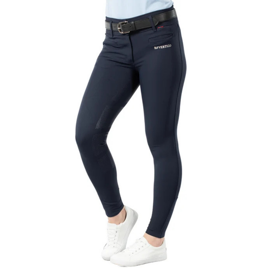 A person wearing navy fitted riding breeches with a black belt and white sneakers, shown from the waist down on a plain white background. A small white logo is visible on the upper right thigh. equestrian fashion outfitters