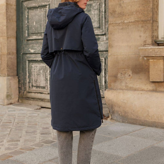 Person wearing a navy blue coat standing in front of a stone building equestrian fashion outfitters