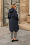 Person wearing a navy blue coat standing in front of a stone building equestrian fashion outfitters