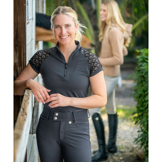 Woman wearing a black equestrian outfit with lace sleeves in an outdoor setting. kastel equestrian fashion outfitters