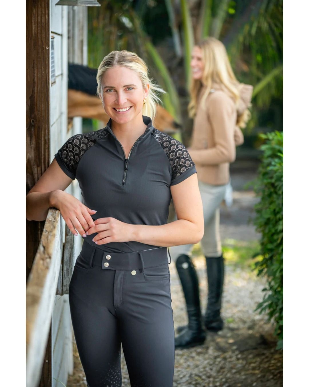 Woman wearing a black equestrian outfit with lace sleeves in an outdoor setting. kastel equestrian fashion outfitters