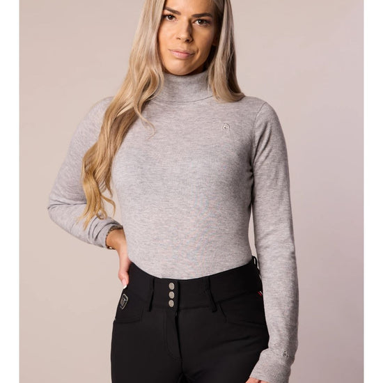 Woman wearing a gray long-sleeve top and black pants against a plain background