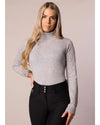 Woman wearing a gray long-sleeve top and black pants against a plain background