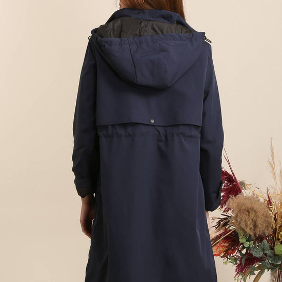 Woman wearing a navy blue hooded coat against a beige background equestrian fashion outfitters