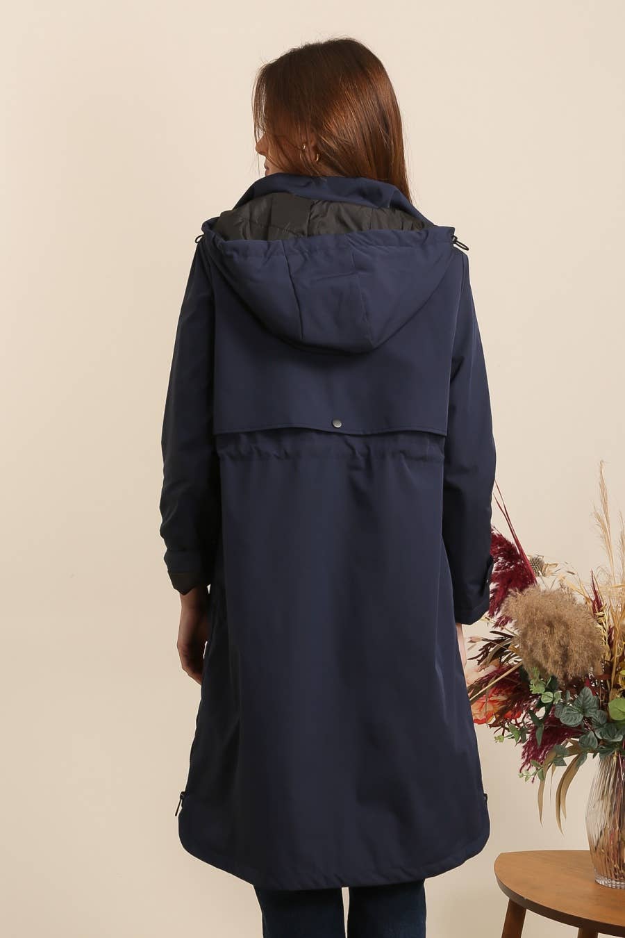 Woman wearing a navy blue hooded coat against a beige background equestrian fashion outfitters