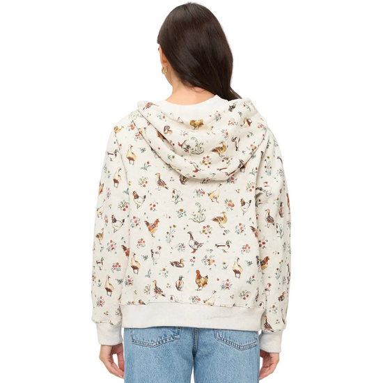 A woman viewed from the back wearing a cream-colored hooded sweatshirt covered in a dense, all-over multicolor print of chickens flowers nature motifs,equestrian fashion outfitters
