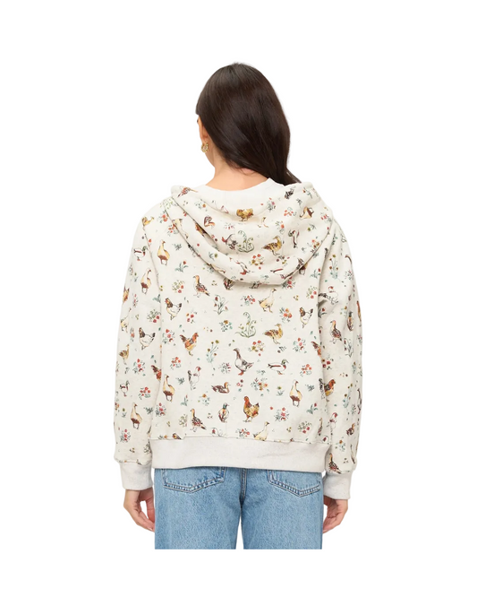A woman viewed from the back wearing a cream-colored hooded sweatshirt covered in a dense, all-over multicolor print of chickens flowers nature motifs,equestrian fashion outfitters