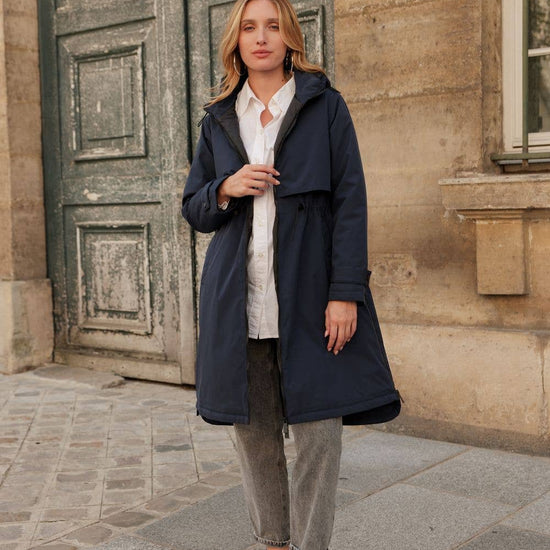 Woman wearing a navy coat standing in front of a stone building. equestrian fashion outfitters