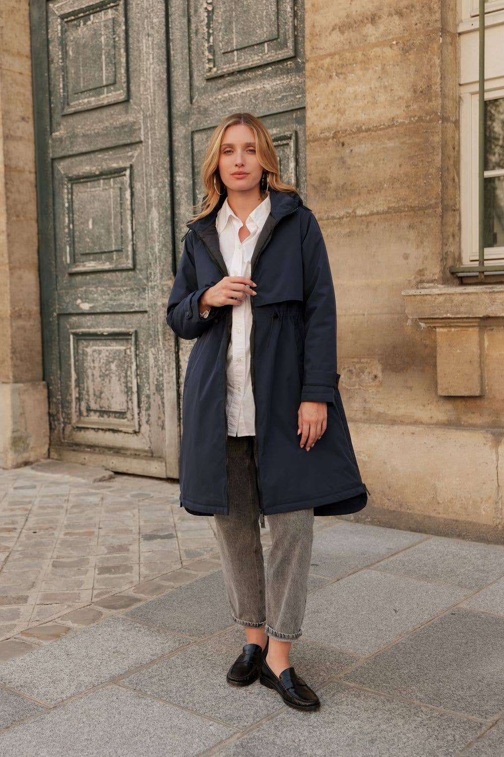 Woman wearing a navy coat standing in front of a stone building. equestrian fashion outfitters