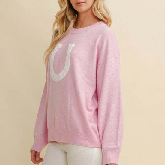 Woman wearing a Pink horseshoe pullover sweater  on a beige background - equestrian fashion outfitters