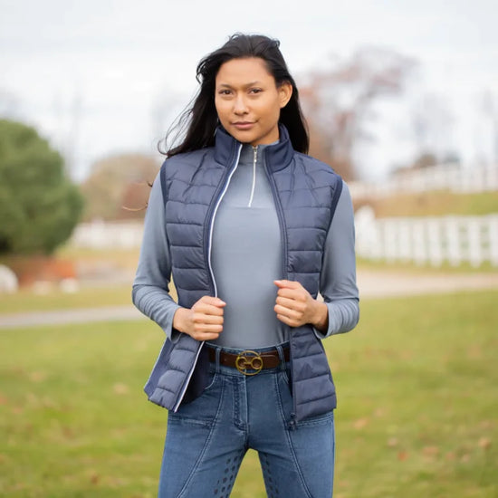 Woman wearing a blue Equinavia Insulated vest outdoors with blurred trees and foliage in the background