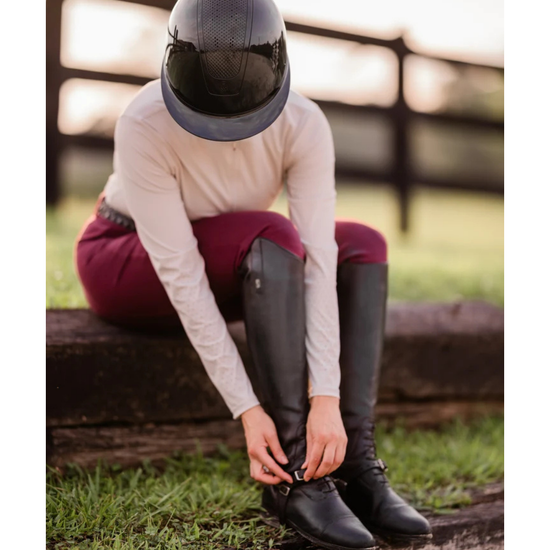 Girl wearing a black glossy  shiny helmet with burgundy breeches tying up her boots equestrian fashion outfitters