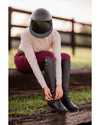 Girl wearing a black glossy  shiny helmet with burgundy breeches tying up her boots equestrian fashion outfitters