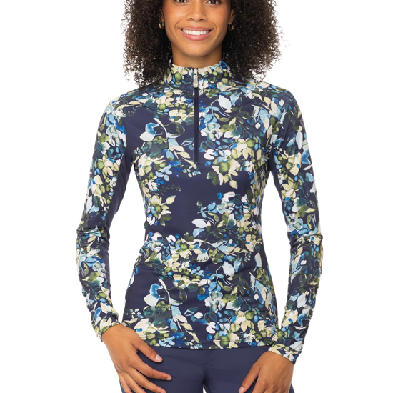 A woman wearing a long-sleeve athletic quarter-zip top with a blue, green, and white floral print, paired with navy blue breeches equestrian fashion outfitters