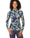 A woman wearing a long-sleeve athletic quarter-zip top with a blue, green, and white floral print, paired with navy blue breeches equestrian fashion outfitters