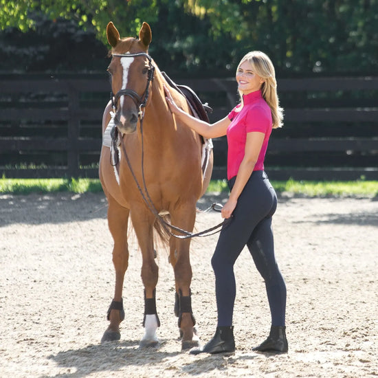 Woman in Horze Grand Prix Knee Patch breeches in Navy Blue with pink shirt standing next to a horse in an outdoor setting