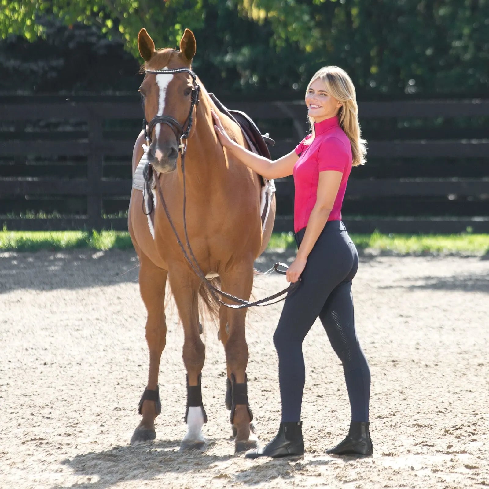 Woman in Horze Grand Prix Knee Patch breeches in Navy Blue with pink shirt standing next to a horse in an outdoor setting