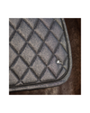 Close-up of a black quilted saddle pad with a diamond pattern and a small white logo, resting on brown fur. equestrian fashion outfitters