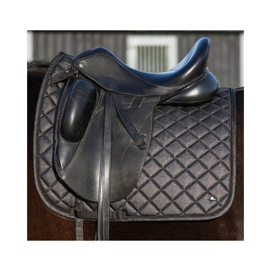 A black leather horse saddle resting on a black diamond-quilted saddle pad, shown against a blurred barn background. equestrian fashion outfitters