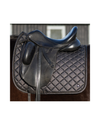 A black leather horse saddle resting on a black diamond-quilted saddle pad, shown against a blurred barn background. equestrian fashion outfitters