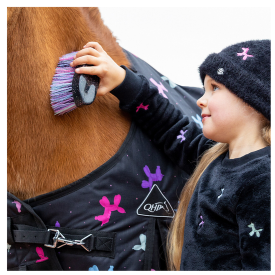 A child wearing a black knit beanie and matching black sweater with colorful motifs gently brushes with a black brush with multi coloured bristles  a brown horse's neck. The horse is wearing a black horse blanket decorated with pink, purple, and blue dog-bone patterns, and a white Q4H! logo is visible on the front.equestrian fashion outfitters