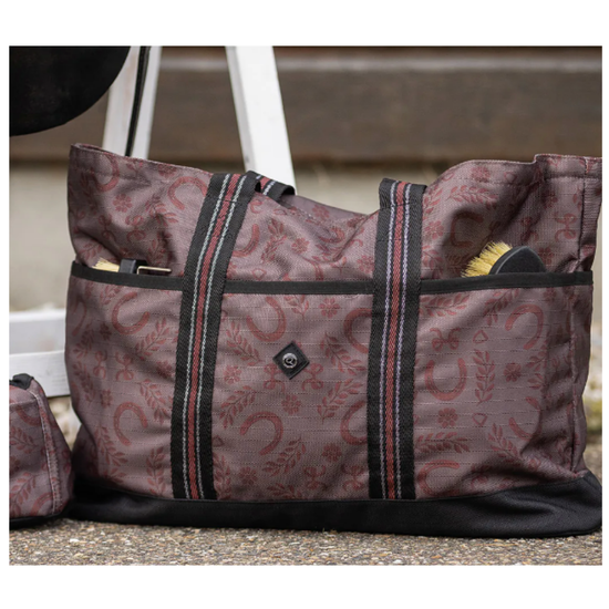 A large tote bag with a brown and red paisley & horseshoe pattern, black trim, and dual shoulder straps, shown outdoors next to a matching small pouch. equestrian fashion outfitters