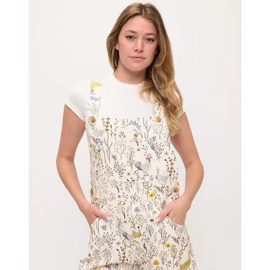 A woman modeling overalls or shortalls with roosters and chickens and flowers on a white background with sneakers equestrian fashion outfitters