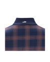 A close-up of a navy blue knit collar with a small white embroidered horse logo, set against a matching navy and peach plaid fabric. equestrian fashion outfitters